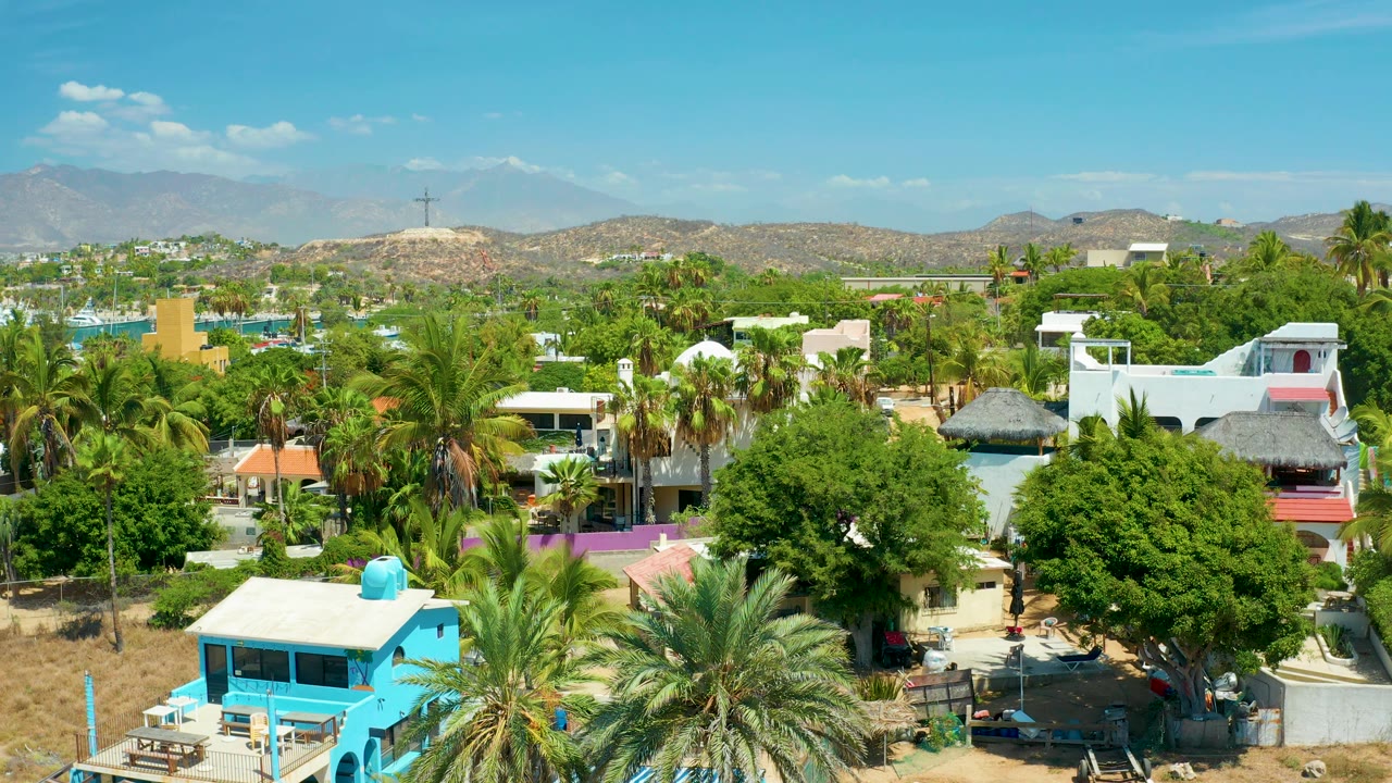 Aerial neighborhood view with colorful buildings, palms, trees, and mountains.