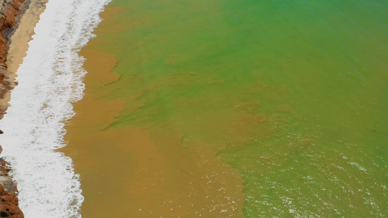 Overhead green sea water and white surf beside sand