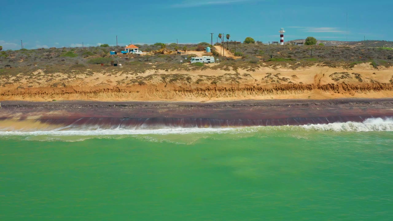 White wave line breaking along a dark beach below dunes