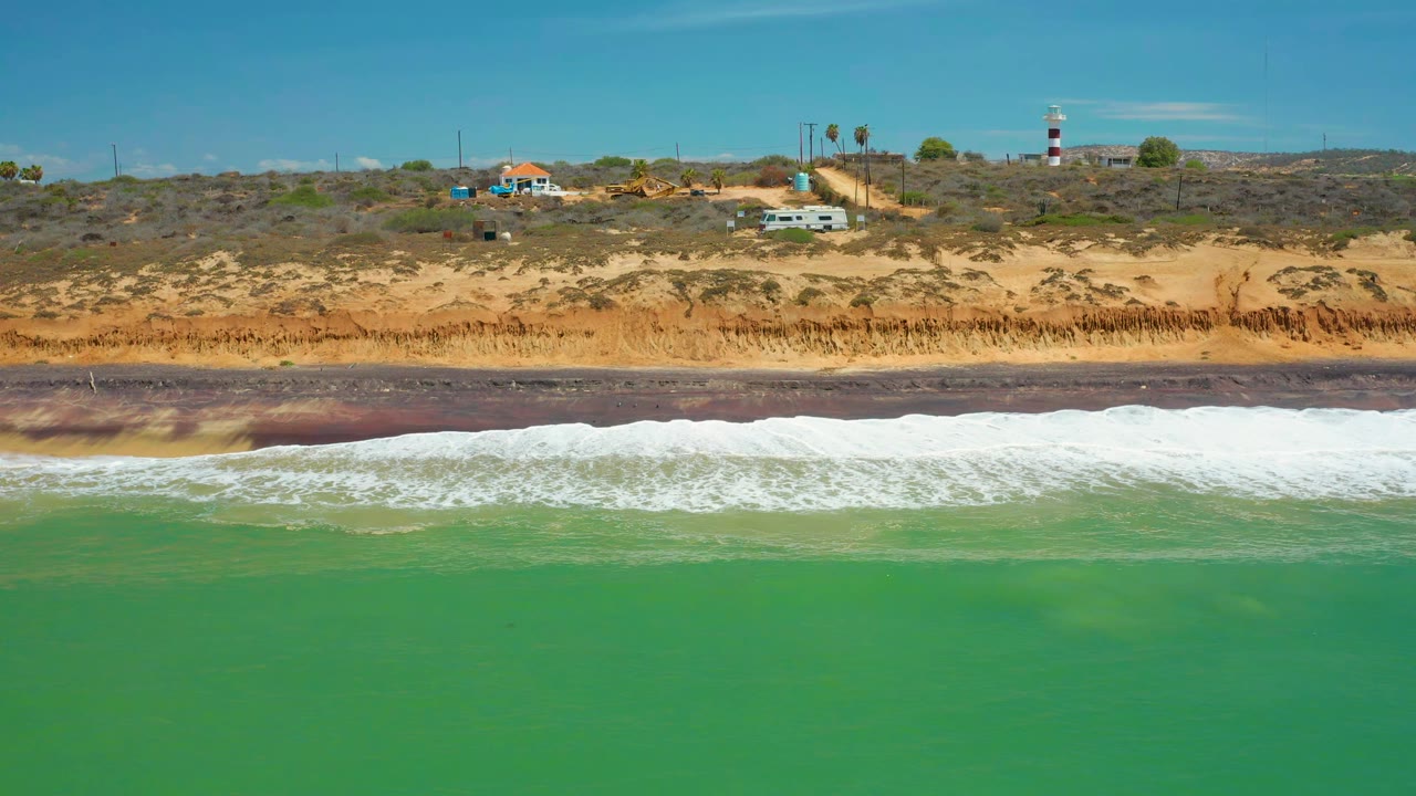 Green water and breaking surf below a scrub-covered sandy cliff.