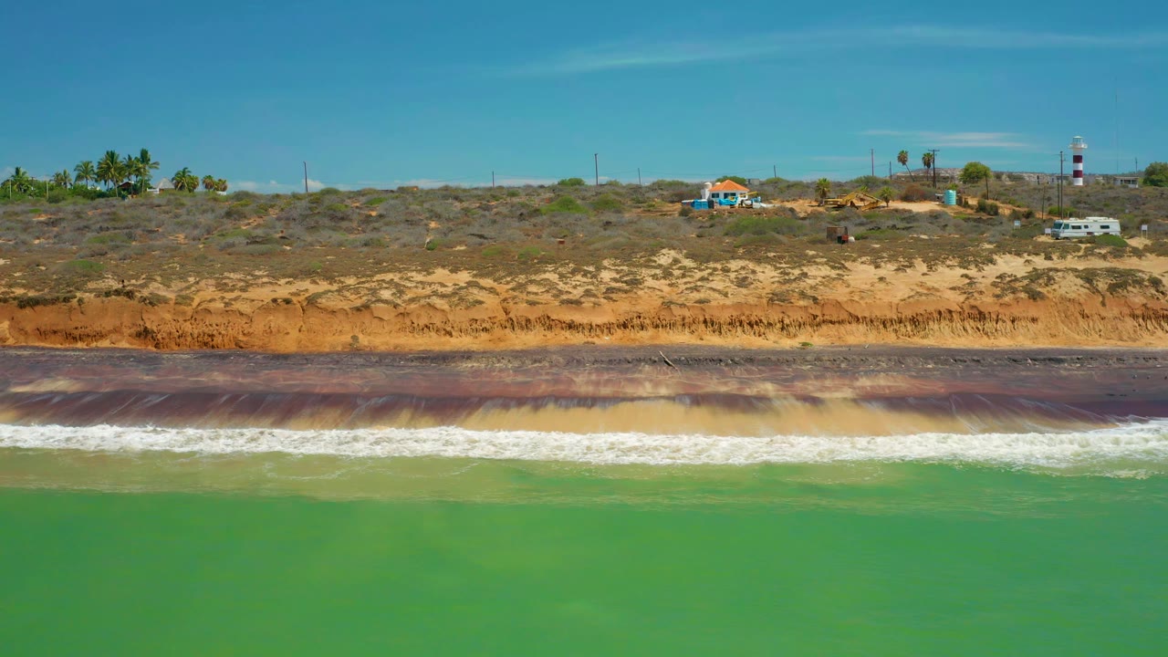 White waves rolling toward a striated brown shoreline
