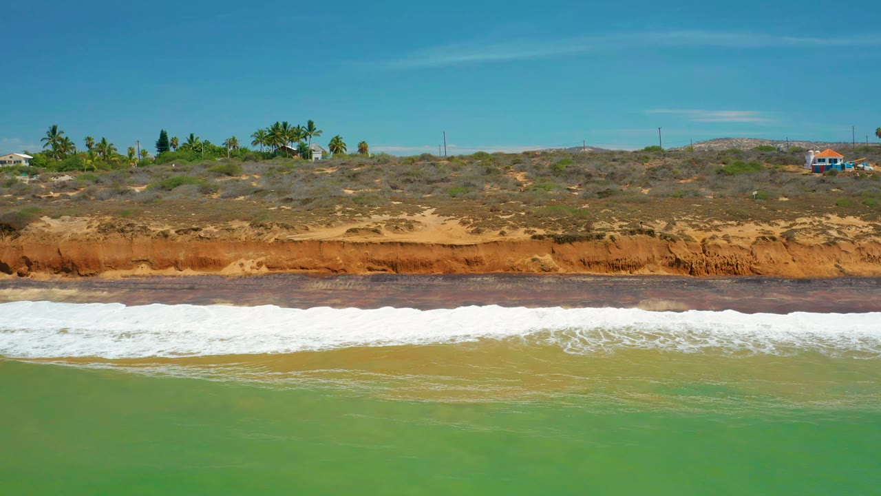White wave spreading across green water in front of coastal bluff