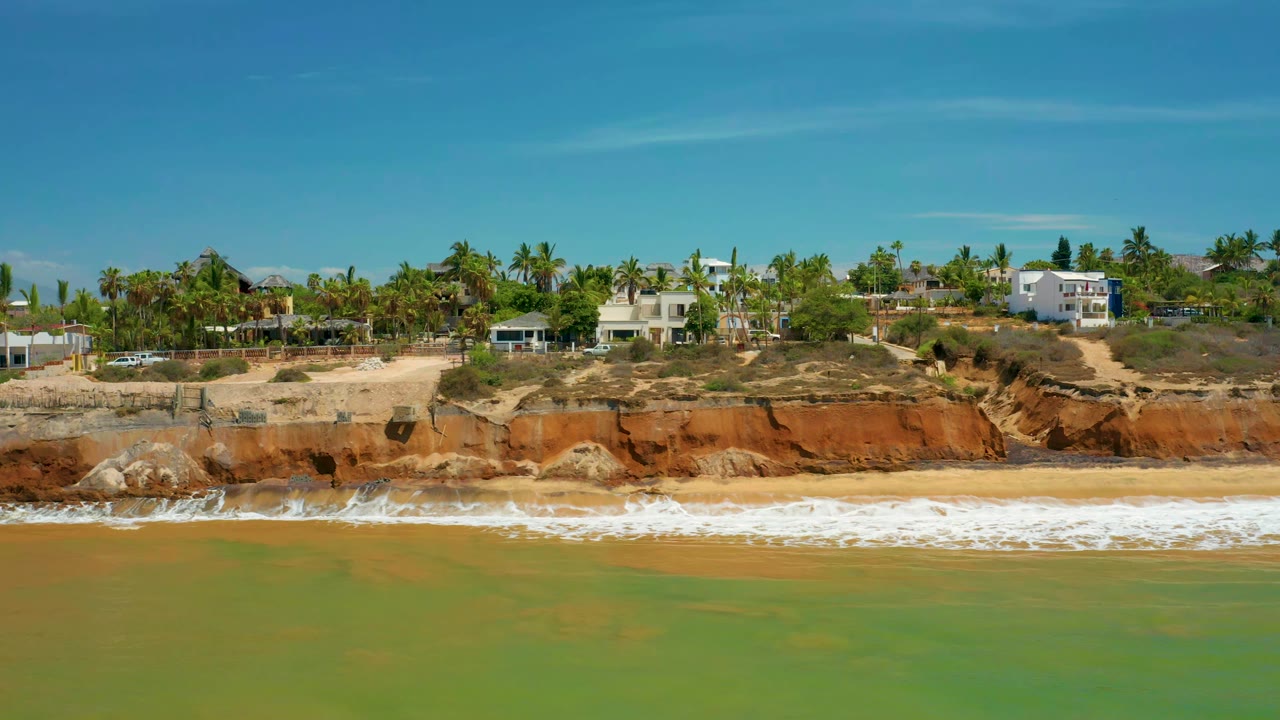 Wide aerial beach view with breaking waves below cliffside homes.