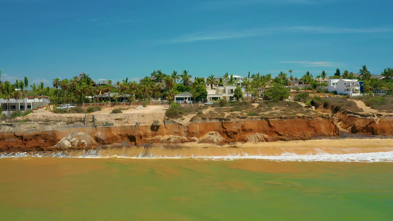 Aerial view of beach surf and eroded cliffs with homes behind.