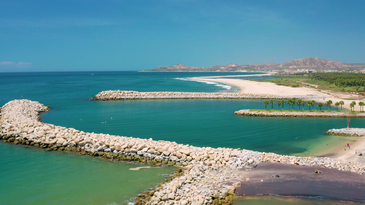 Aerial view of a rock breakwater beside turquoise water and a sandy beach.
