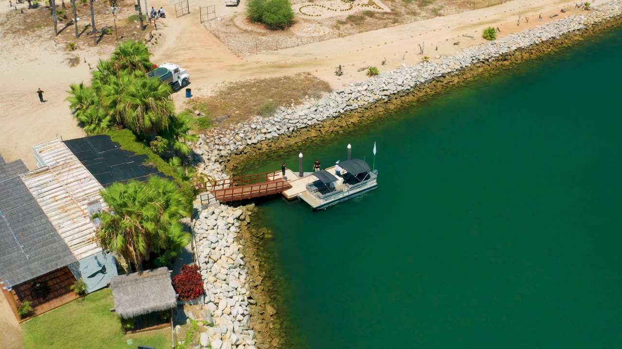 Aerial view of the dock and boat with palms and rocks along the shore.