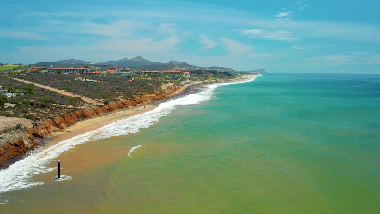 Aerial coastline with turquoise sea, surf, cliffs, and distant hills