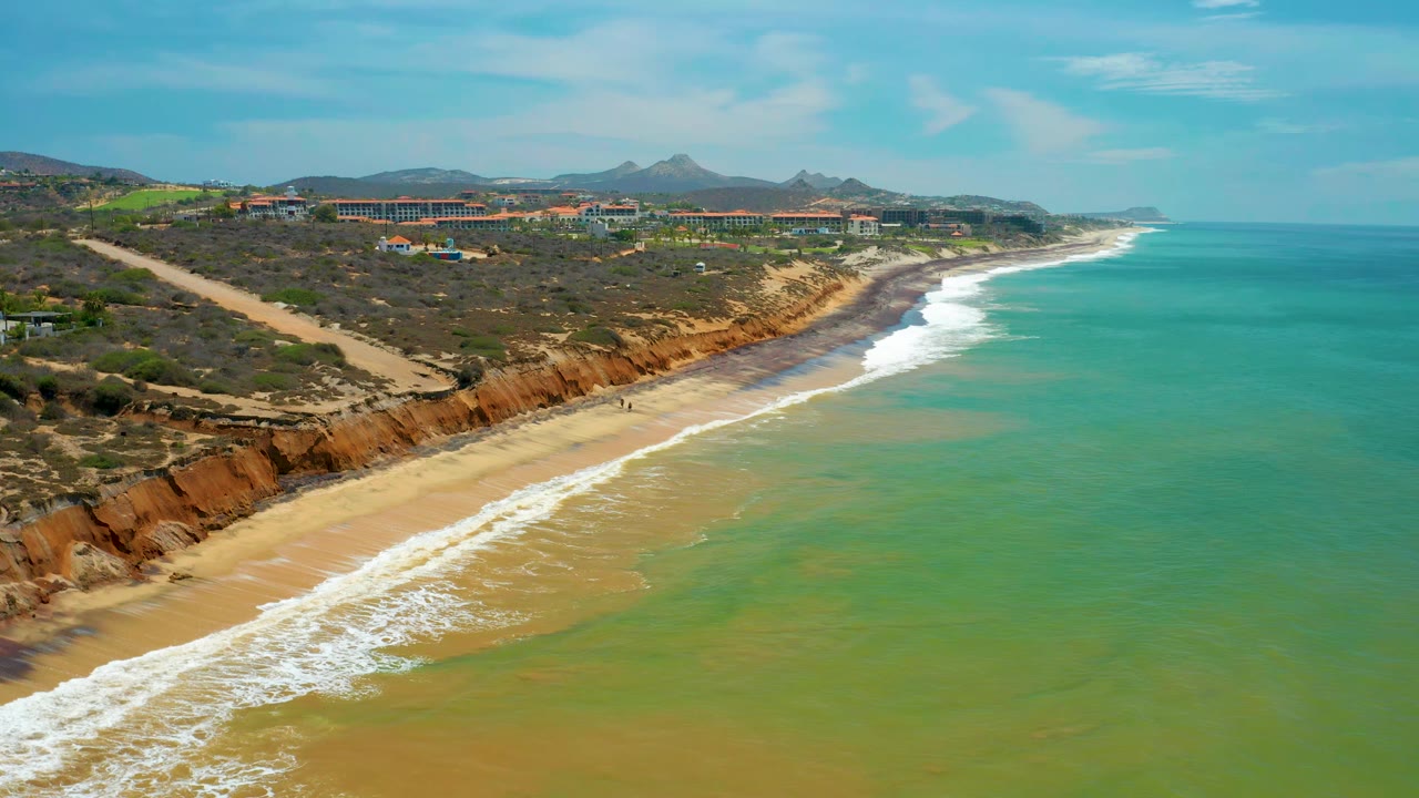 Aerial beach view with waves breaking beside rust-colored cliffs.