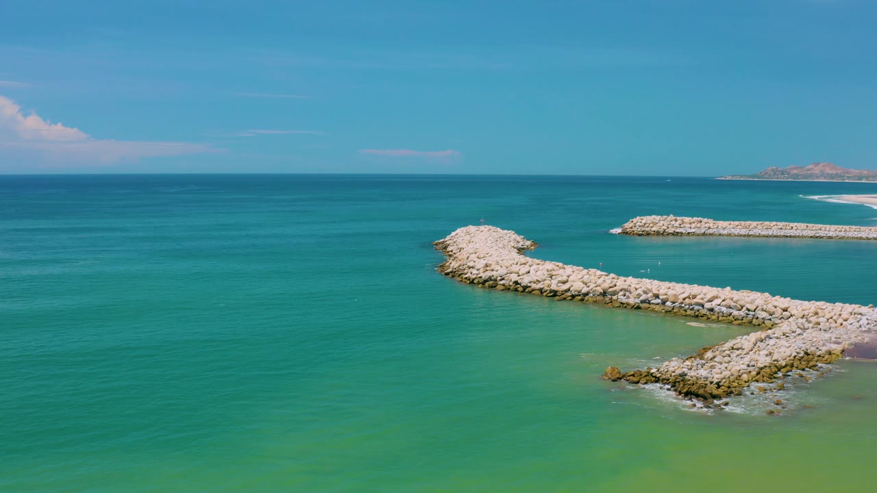 Aerial coastal view in San Jose Del Cabo, Mexico with calm blue water, green shallows near the lower edge, pale rock arms, and no visible people.