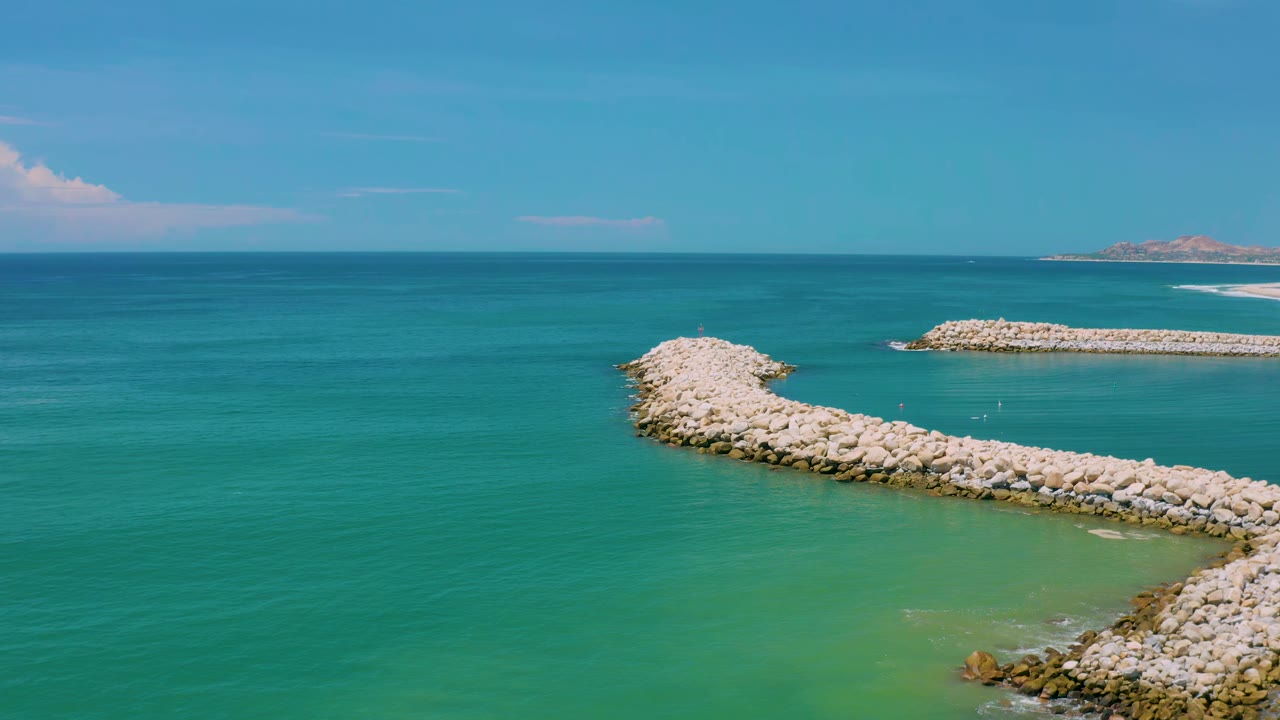 Aerial coastal view with breakwaters and calm teal water.