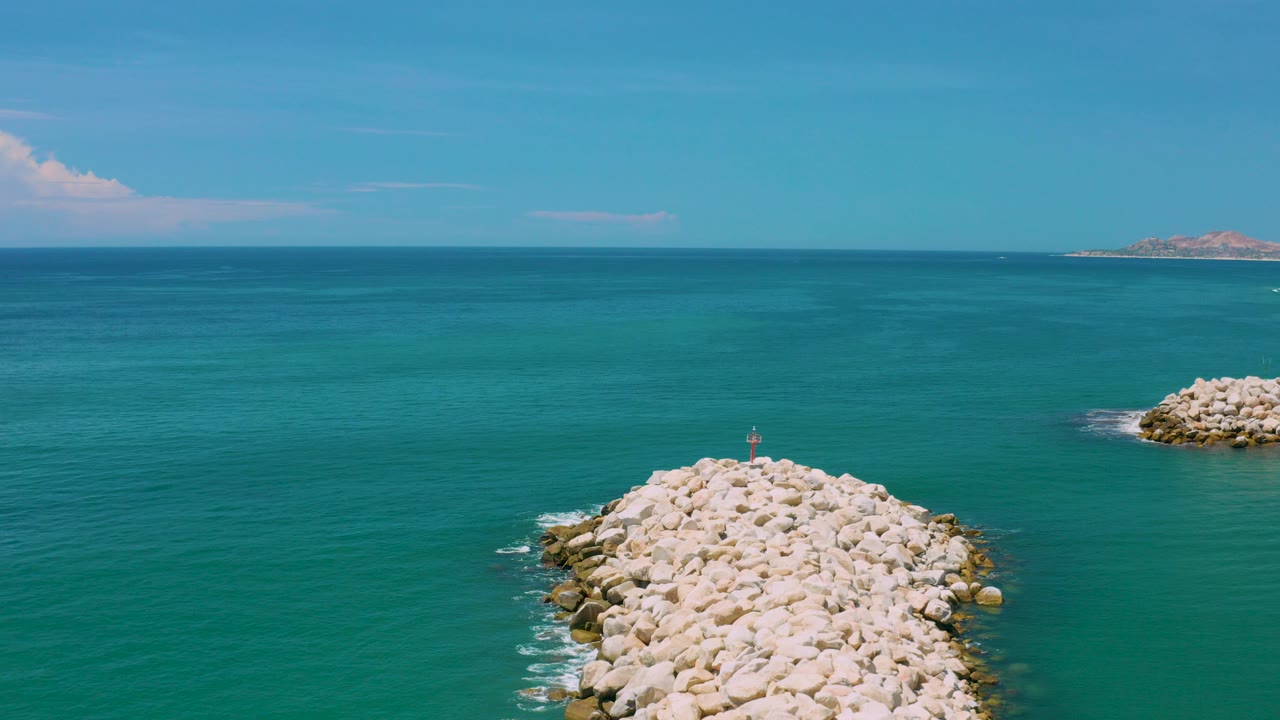Aerial ocean view with a pale rock breakwater below a blue sky.