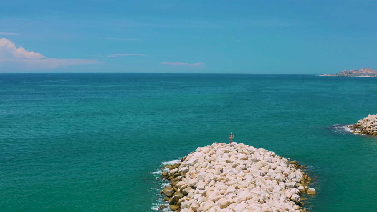 San Jose Del Cabo view with the breakwater lower in the frame, a large expanse of blue water, soft clouds to the left, distant land to the right, and no visible people.