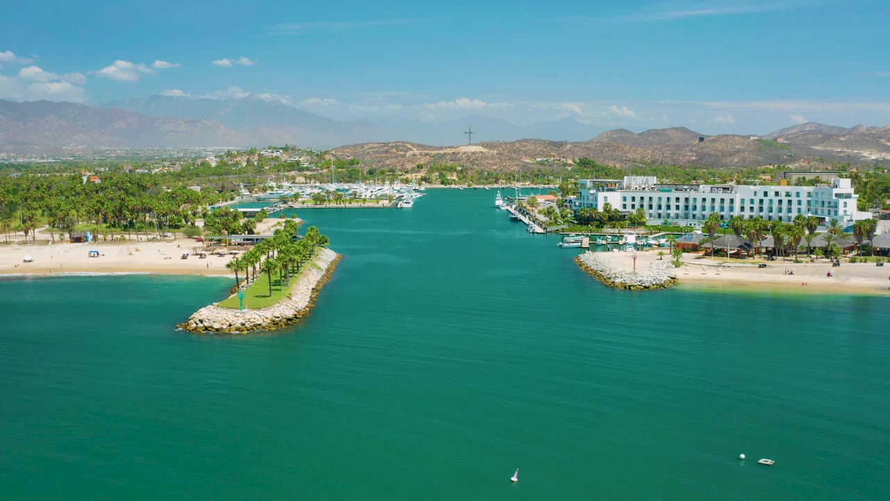 Drone view facing a resort beach with palm-lined breakwaters and calm open water in front.