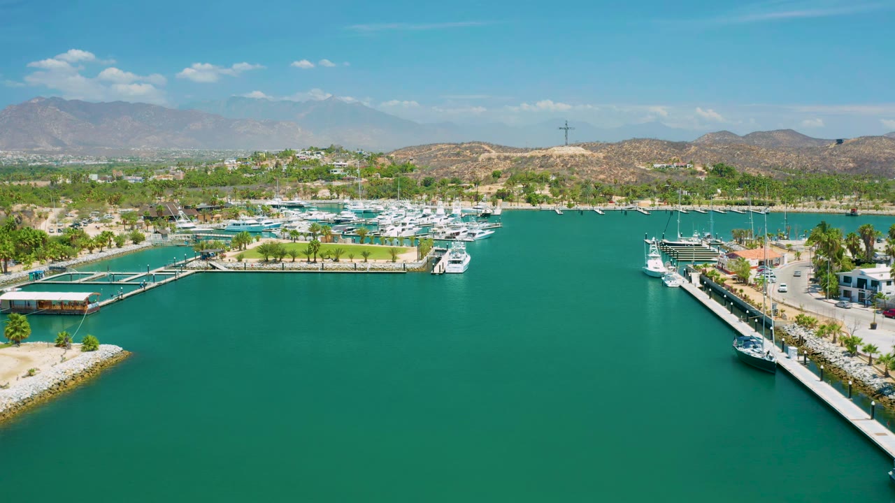 Aerial view in San Jose del Cabo, Mexico, with open green water filling the foreground, a marina basin and moored boats across the center, low hills behind, and no visible people.