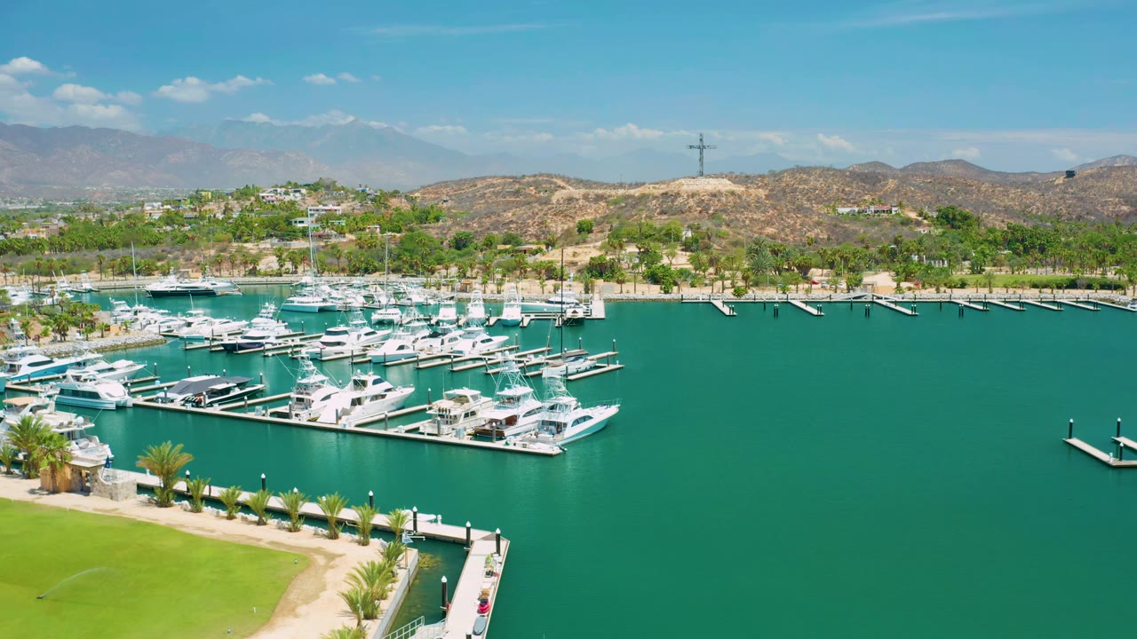 White yachts clustered at marina docks beside open green water and hills.