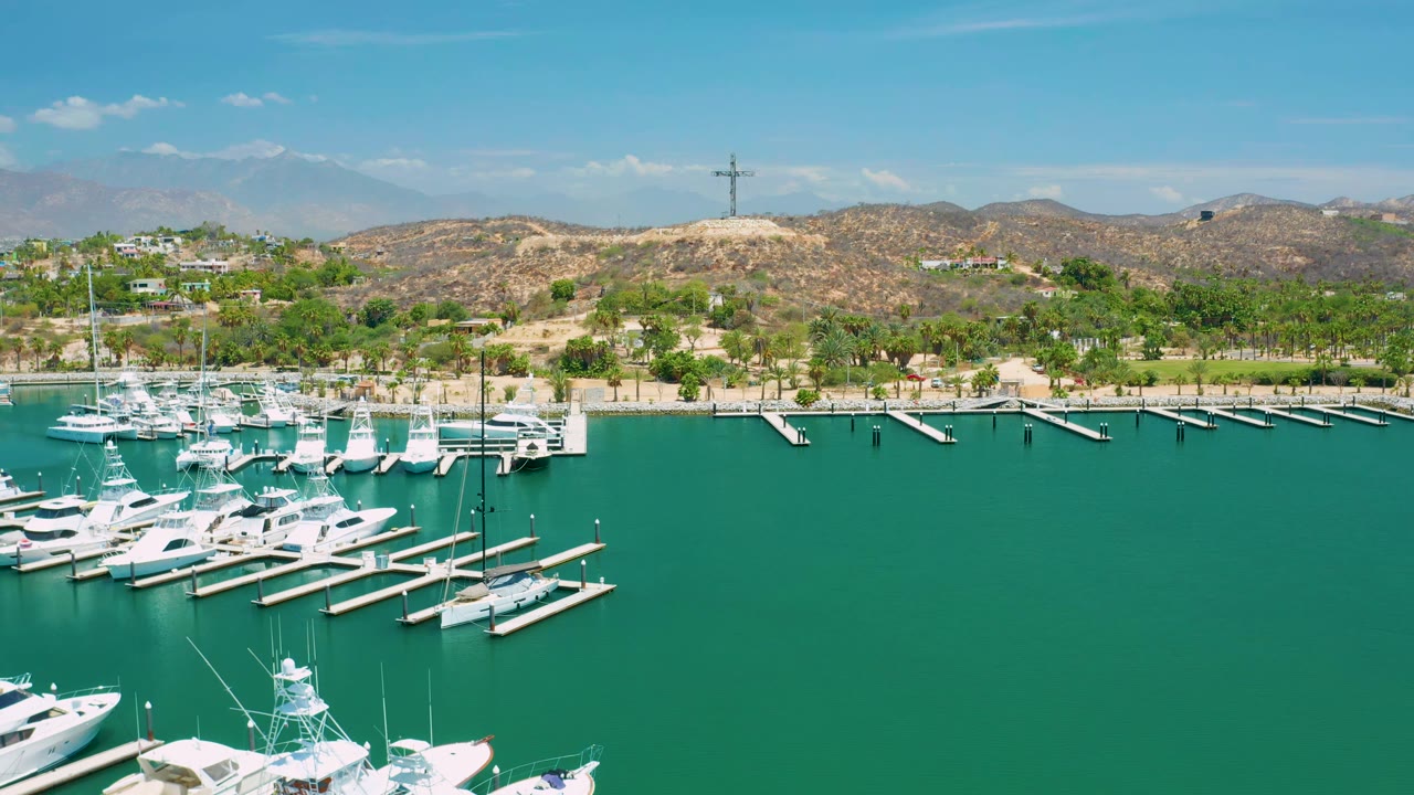 Wide aerial marina view with empty slips, clustered boats, shoreline trees, and hills.