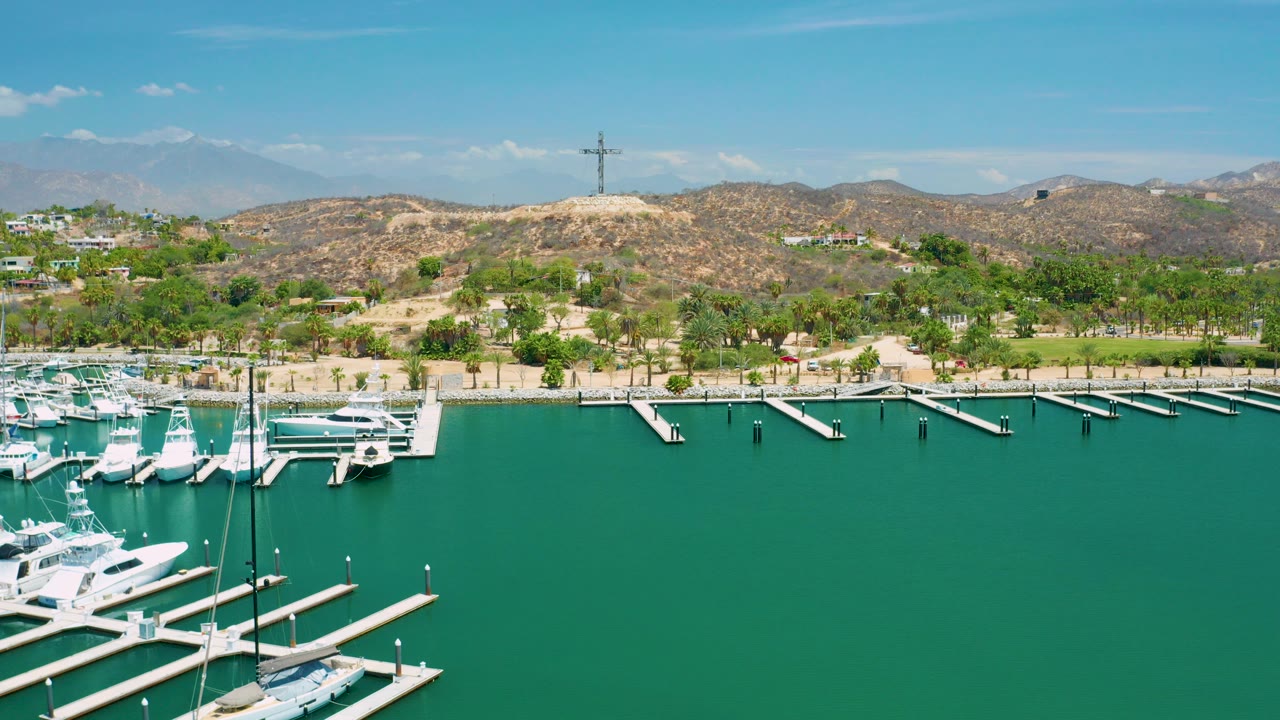 Aerial view of green marina water with white boats, docks, shoreline palms, and dry hills.
