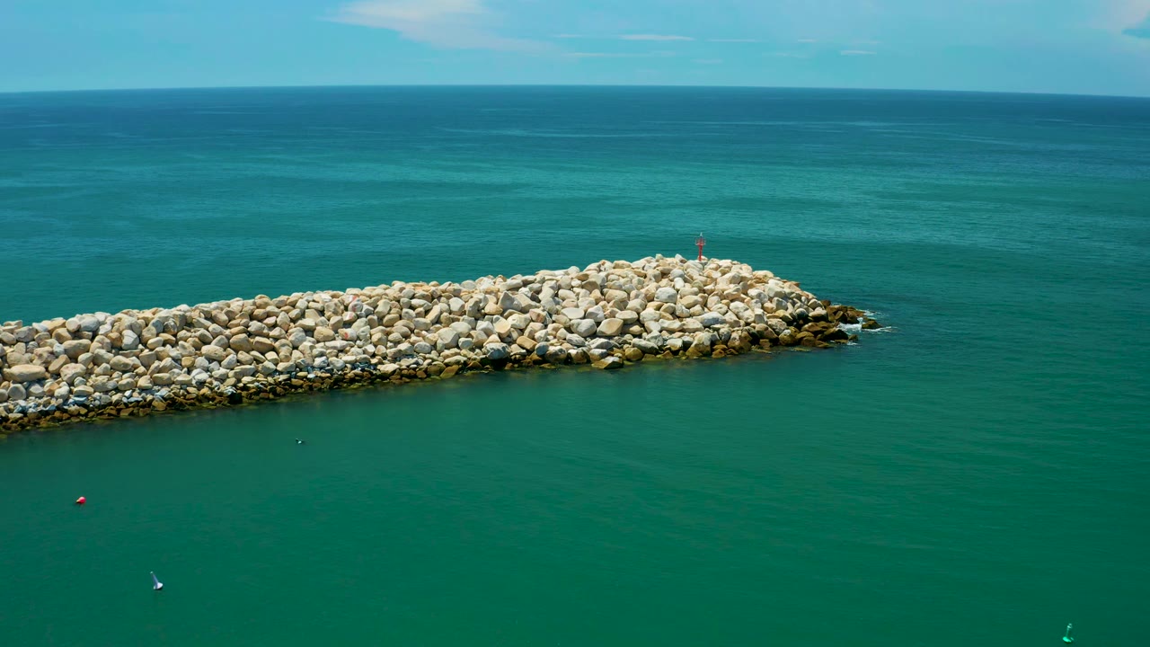 Rock breakwater crossing teal ocean under a level horizon.