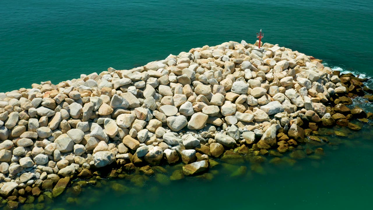 Closer aerial view of the San Jose del Cabo breakwater, where large pale boulders fill most of the frame and green water borders the lower edge, with no visible people.