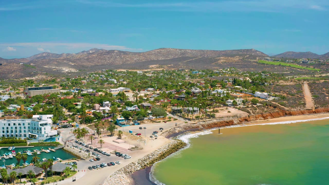 Aerial coastline with marina, white waterfront building, town, and hills