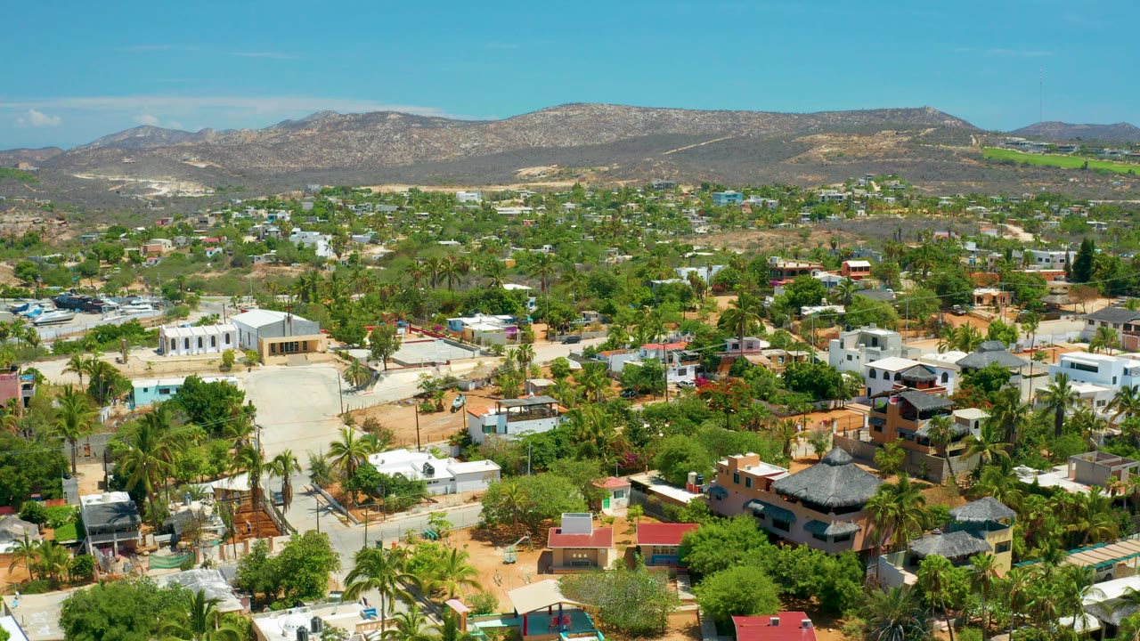 Aerial neighborhood view with white buildings, palms, and hills.