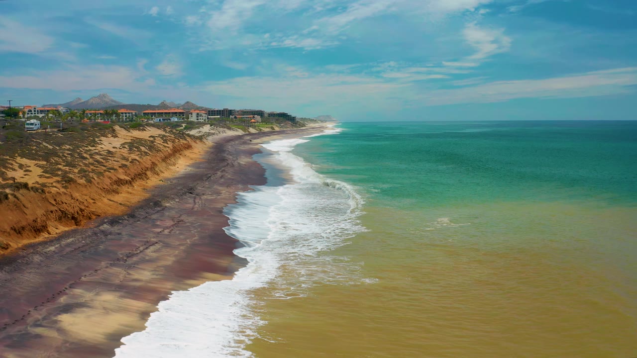 High coastal view with waves breaking beside a cliff-backed beach.