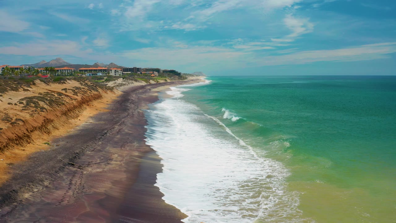 Aerial view down a curving beach with surf and bluff-top buildings