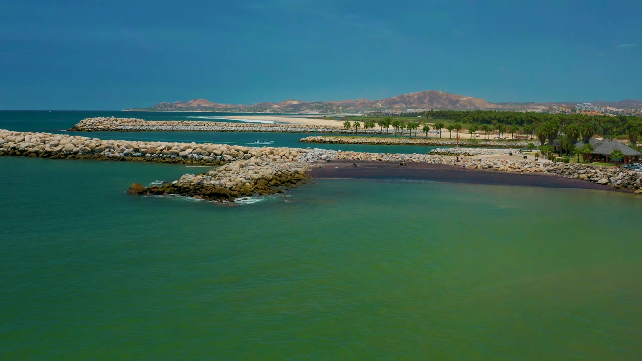 Wide coastal aerial with a rocky jetty extending into green water.