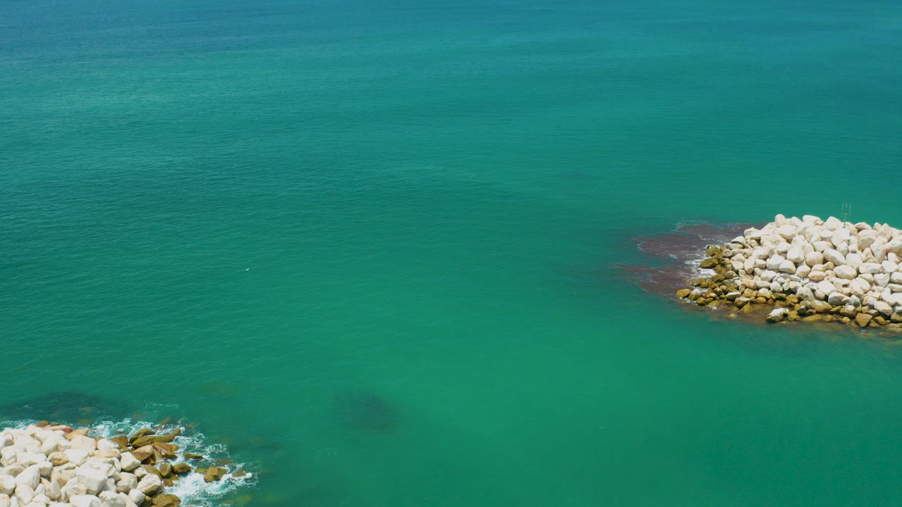 Overhead view of green-blue ocean near San Jose Del Cabo, Mexico, with pale rock piles partly entering the lower left and upper right edges and no visible people.