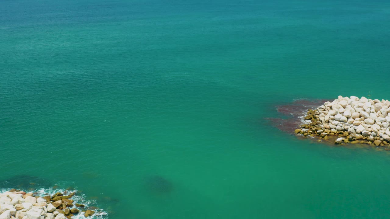 The rock mound shifts close to the top-right edge over green-blue water near San Jose Del Cabo, Mexico, with faint underwater shadows and no visible people.