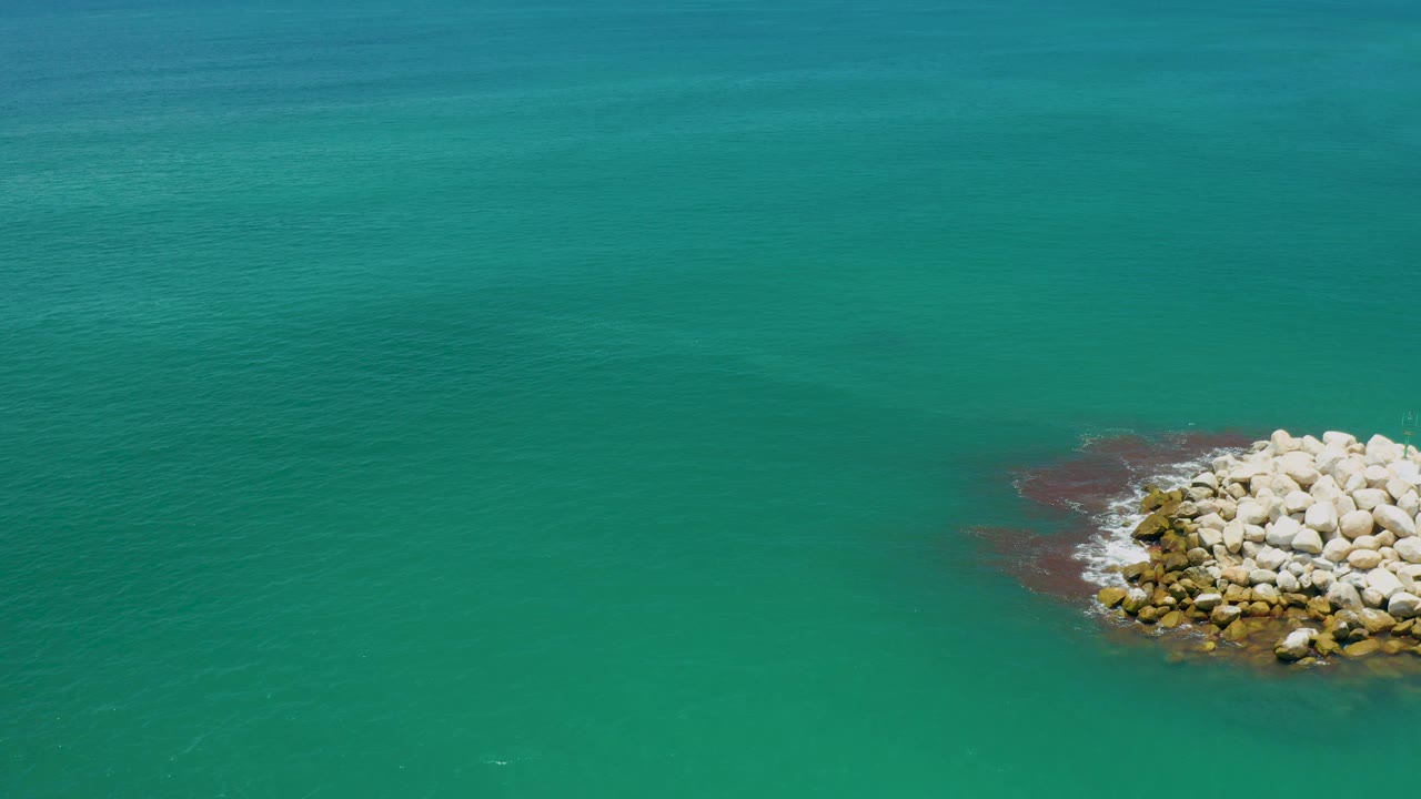 Aerial view in San Jose del Cabo, Mexico, with the white rock pile near the far right edge, teal water across the frame, and no visible people.