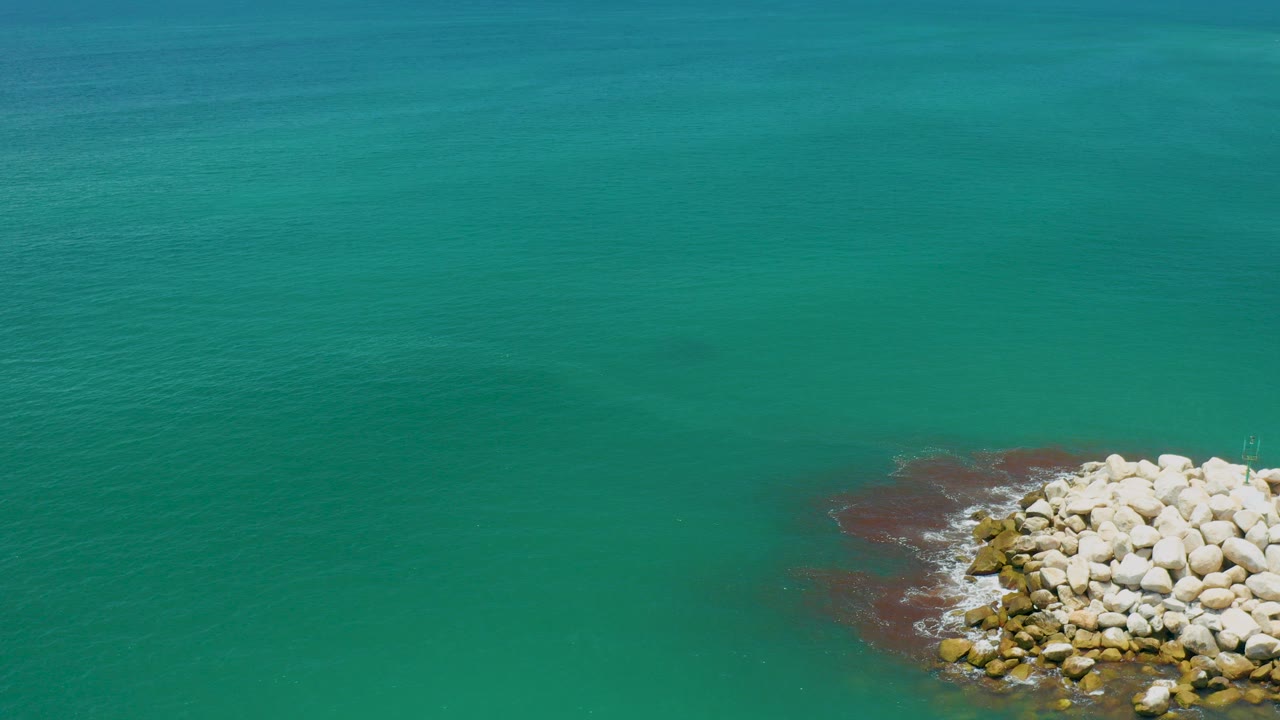 Aerial view of turquoise sea in San Jose Del Cabo with pale rocks entering from the lower right and no visible people.