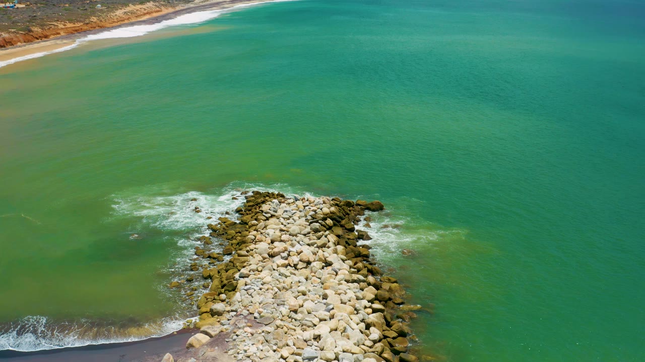 Rocky boulder formation surrounded by foam in green turquoise water.