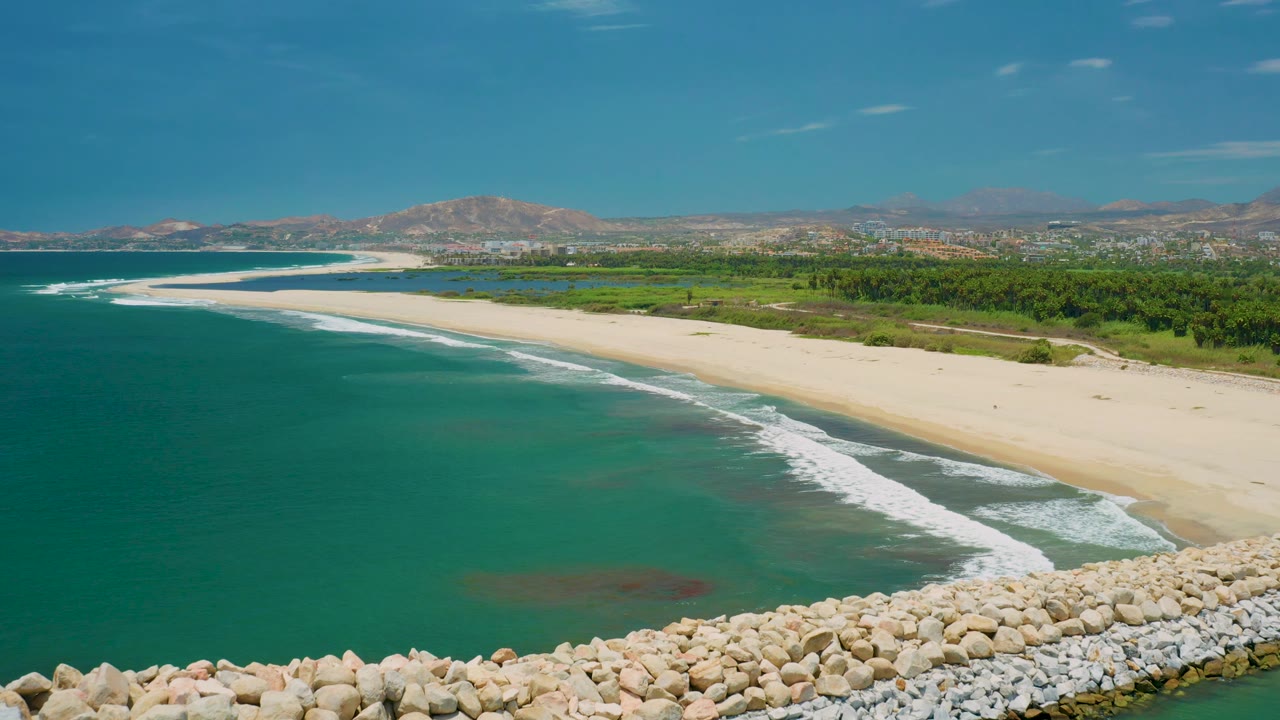 Wide beach and surf viewed from above with rocks at the bottom and mountains beyond.