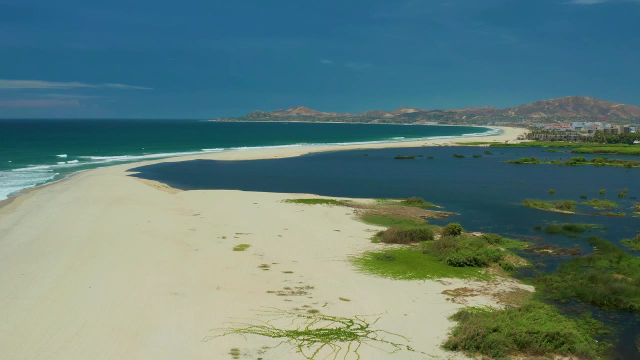 White sand beach with ocean surf on the left and wetland on the right.