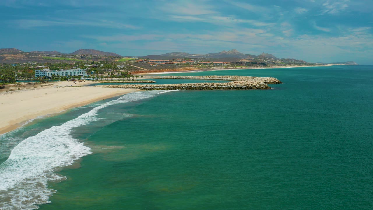 Aerial view of turquoise ocean washing onto a sandy beach beside a rock jetty.