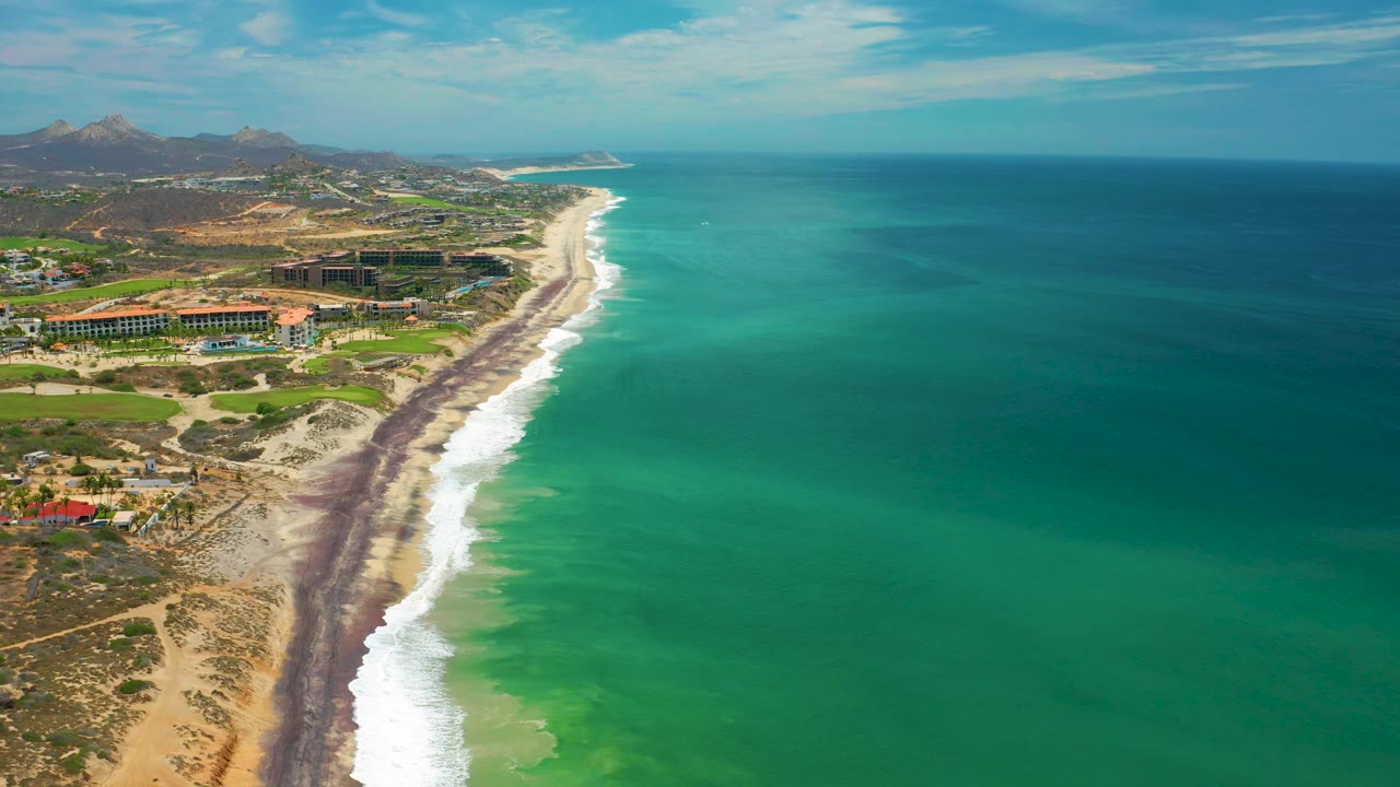 Aerial beach and ocean view with buildings on the inland side.