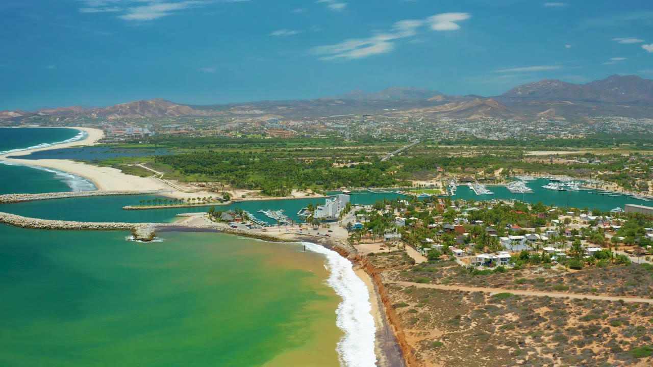 Elevated coastline view with beach curve, breakwater, marina, greenery, and mountains