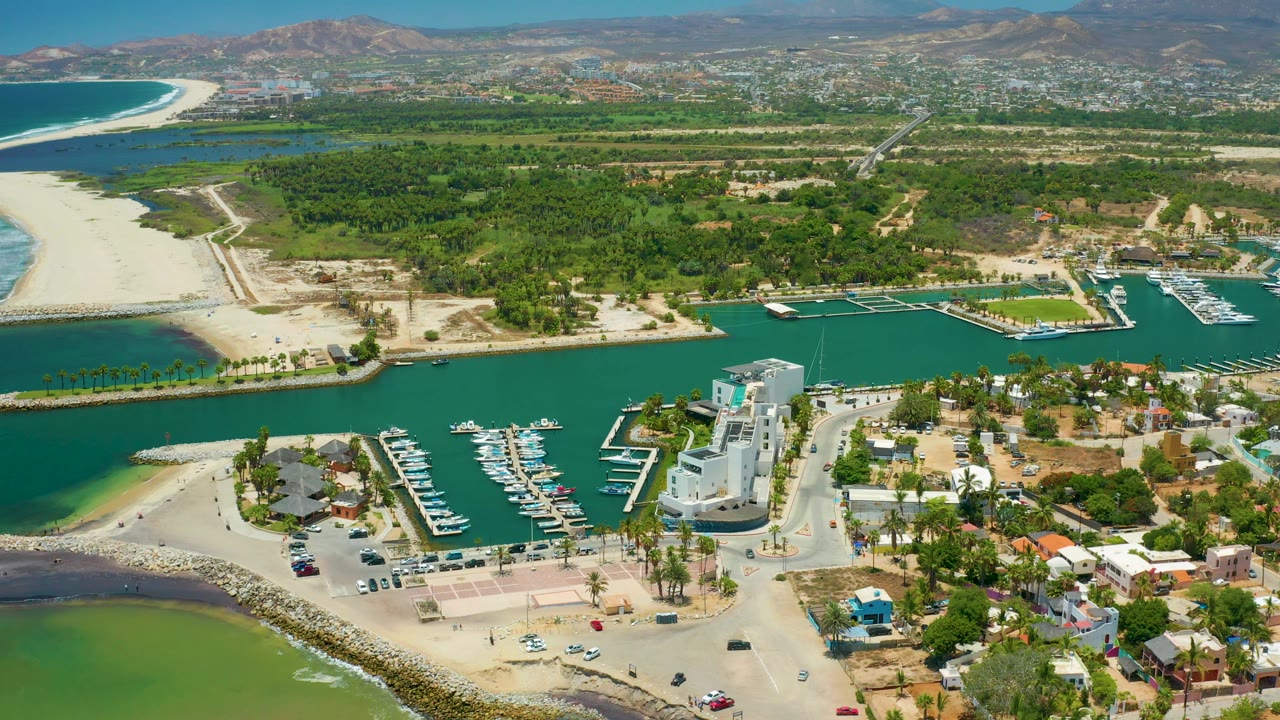 Aerial marina scene with boats, breakwater, beach, and hills.