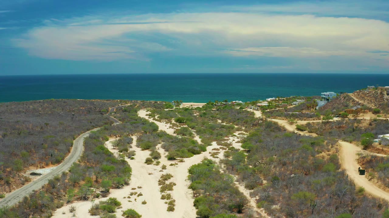 Wide aerial coastline with sand washes, brush, road, and blue sea.