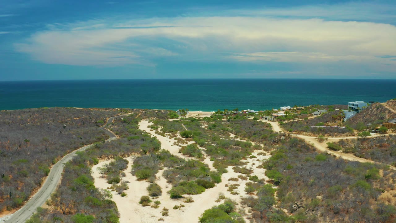 Wide aerial coastline with desert brush, beach houses, and calm blue sea.