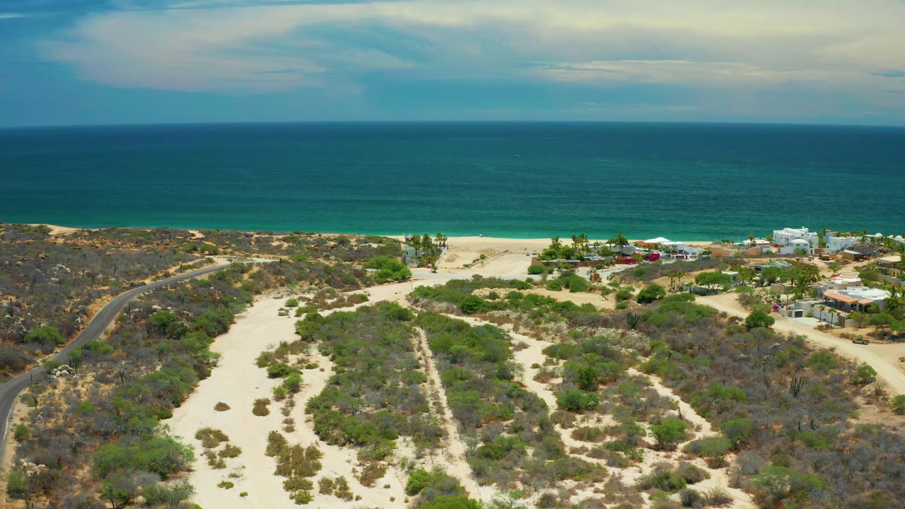 San Jose Del Cabo coastline seen from above, with winding sandy tracks through scrub, a narrow beach band, blue-green water, and no visible people.