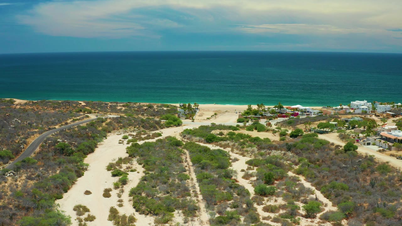 Aerial beach view with desert brush, sandy washes, ocean, and distant buildings.