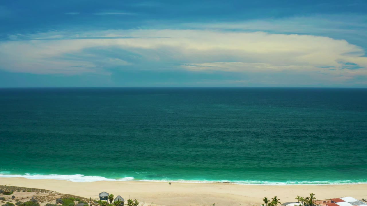 San Jose Del Cabo shoreline seen from above with the horizon high in frame, teal water filling the center, thin white surf at the sand, and no visible people at 0:01.