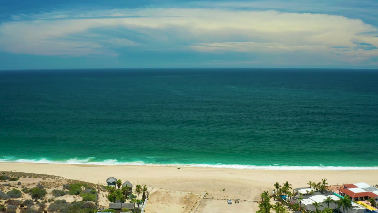 Elevated San Jose del Cabo beach frame with open sand in the lower third, dark-to-light ocean color bands, a thin surf edge, and no visible people.