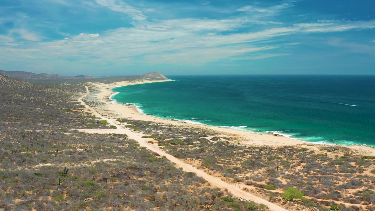 Aerial view of a curved beach and blue ocean beside dry scrubland.