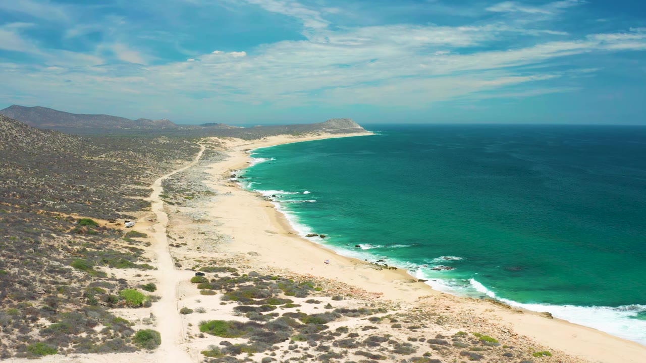 High aerial view of waves lapping a long beach beside scrubland.