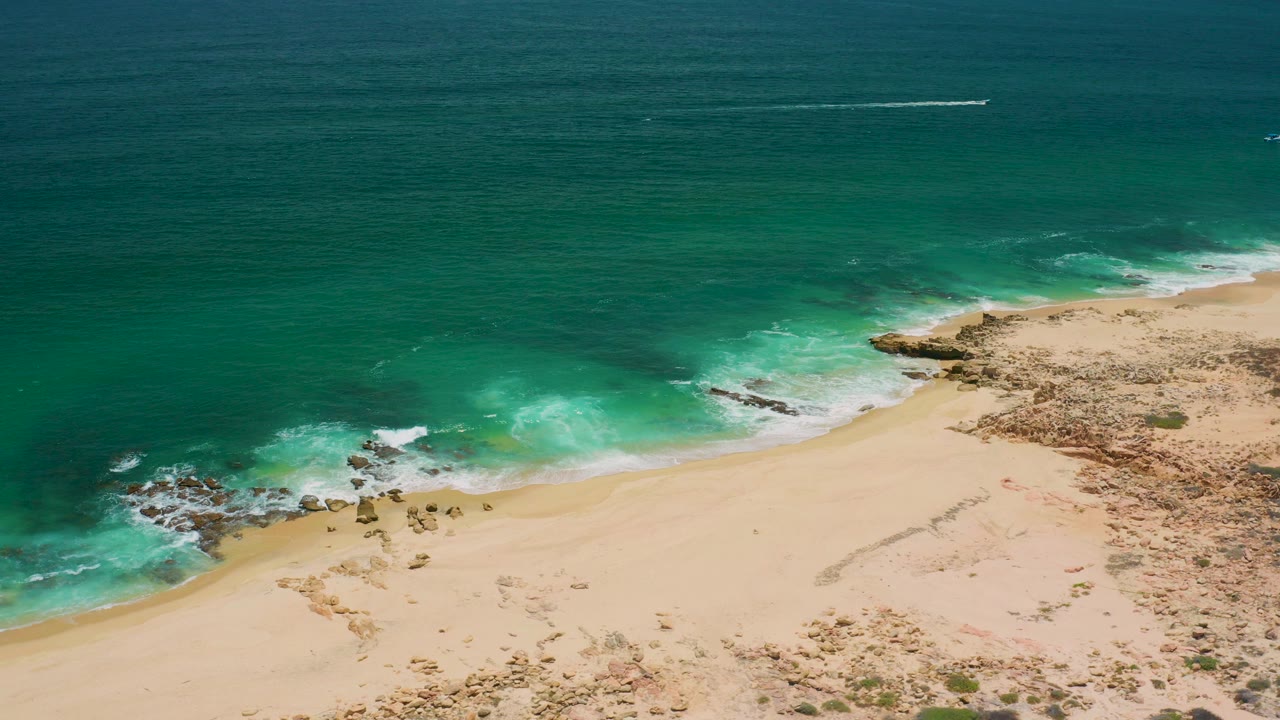 Aerial frame over a San Jose del Cabo beach where turquoise water breaks against rocks and pale sand, with no visible people.