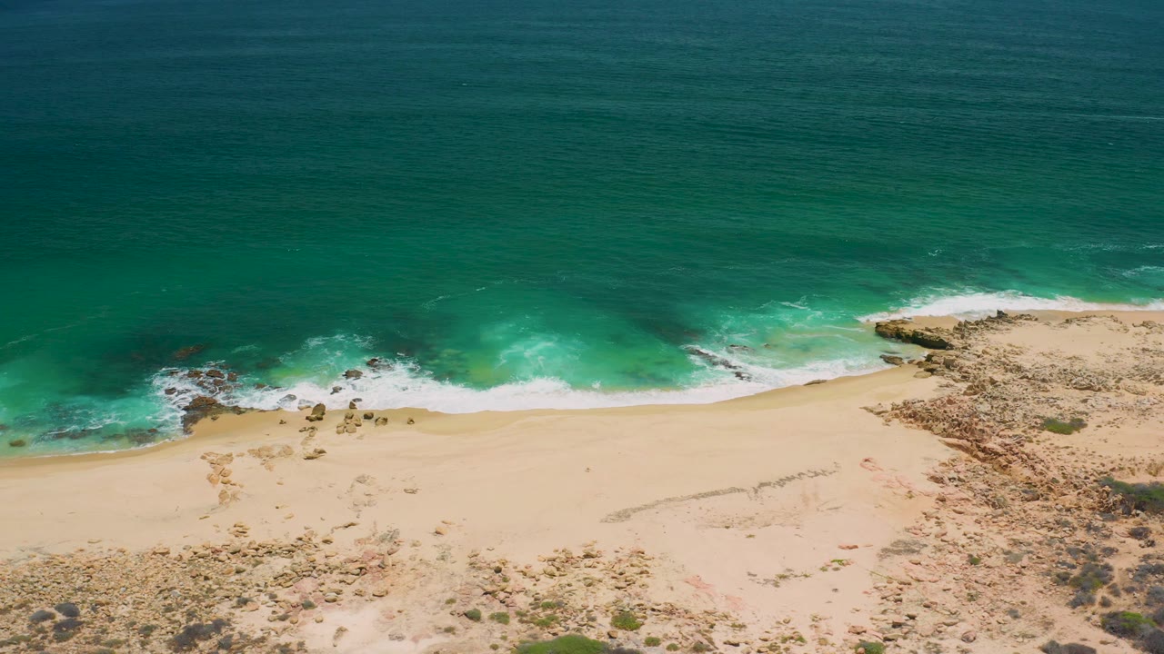Overhead beach and ocean with surf curling along pale sand.