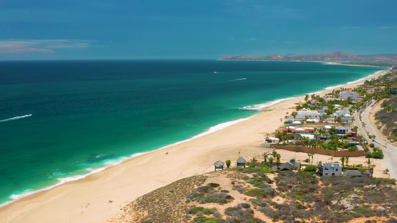 Wide aerial view of surf, open ocean, beach homes, and coastal road.